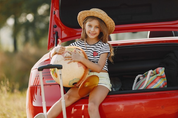 Kleines Mädchen bereit, in den Urlaub zu fahren. Kind in einem roten Auto. Mädchen mit Globus und Hut.