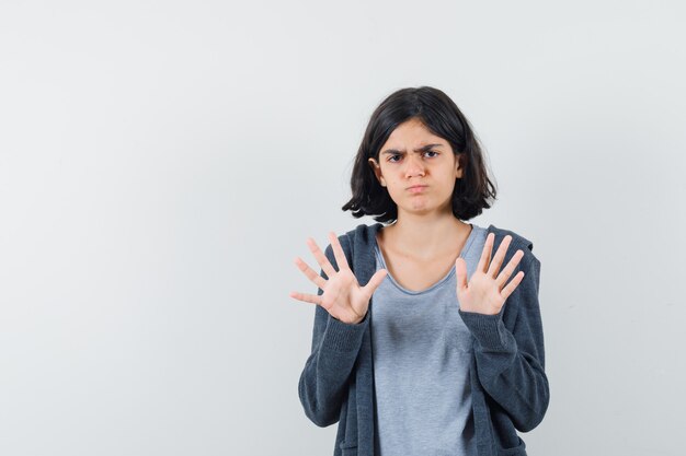 Kleines Mädchen, das Ablehnungsgeste in T-Shirt, Jacke zeigt und genervt aussieht