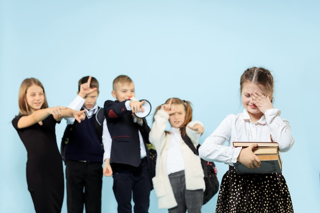 Kleines Mädchen, das allein auf Stuhl sitzt und einen Akt des Mobbings erleidet, während Kinder verspotten