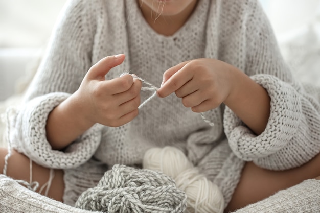 Kleines Mädchen, das auf dem Sofa sitzt und lernt, zu stricken, Freizeitkonzept zu Hause.