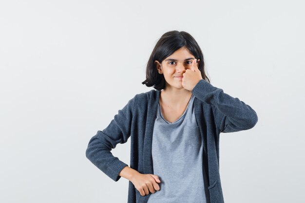 Kleines Mädchen, das Daumen oben in T-Shirt, Jacke zeigt und glücklich schaut