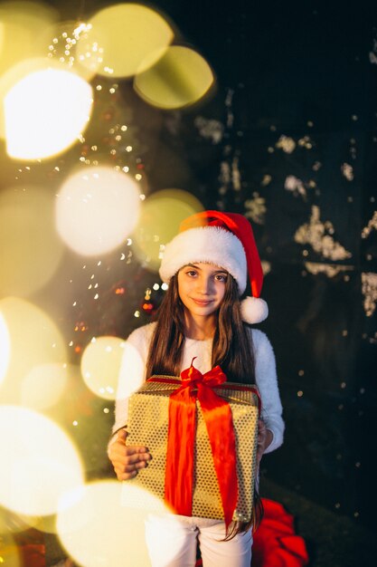 Kleines Mädchen, das durch Weihnachtsbaum sitzt und Geschenke auspackt