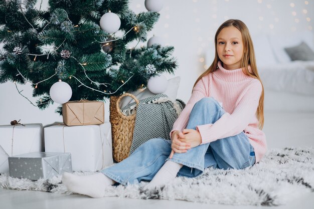 Kleines Mädchen, das durch Weihnachtsbaum sitzt