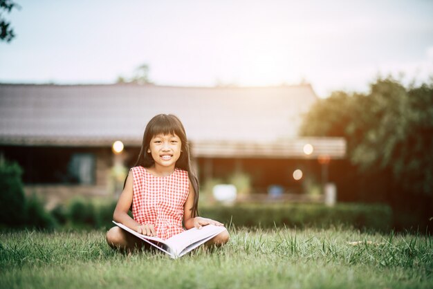 Kleines Mädchen, das ein Buch im Hausgarten liest