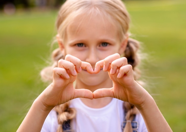 Kostenloses Foto kleines mädchen, das ein herz mit ihren fingern zeigt