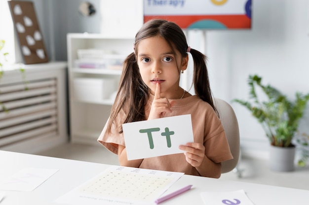 Kleines Mädchen, das ein Papier mit einem Buchstaben in der Logopädie hält