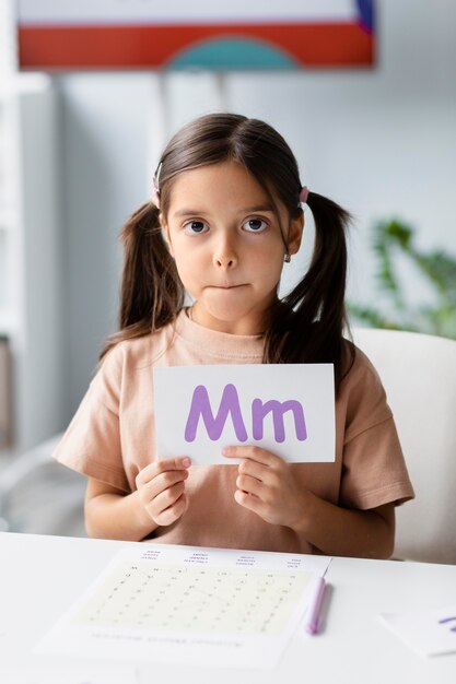 Kleines Mädchen, das ein Papier mit einem Buchstaben in der Logopädie hält