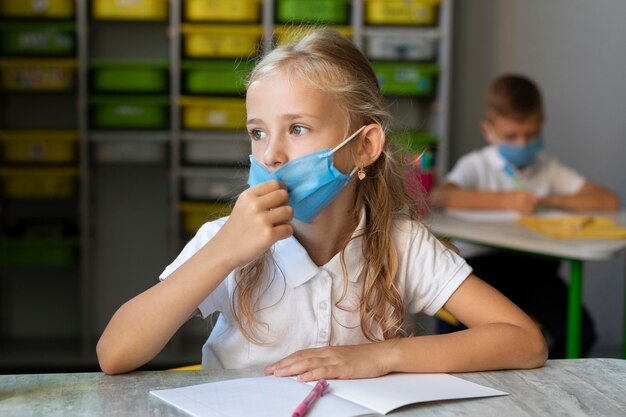 Kleines Mädchen, das eine medizinische Maske im Unterricht trägt