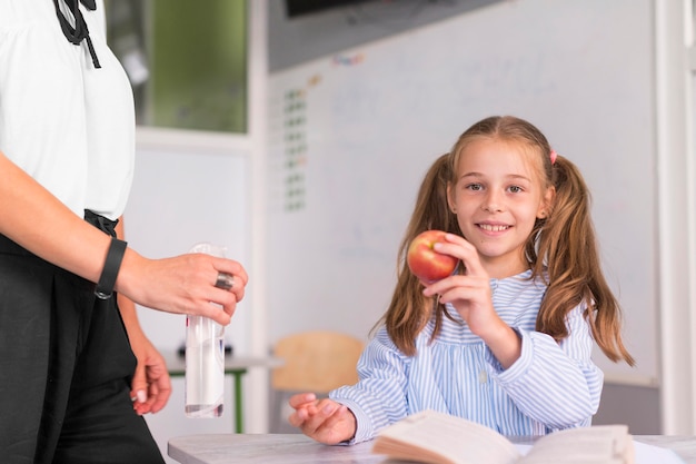 Kleines Mädchen, das einen Apfel neben ihrem Lehrer hält