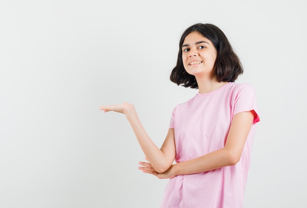 Kleines Mädchen, das etwas zeigt oder im rosa T-Shirt begrüßt und fröhlich, Vorderansicht schaut.