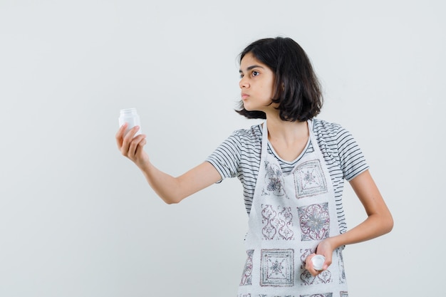 Kleines Mädchen, das Flasche Pillen im T-Shirt präsentiert