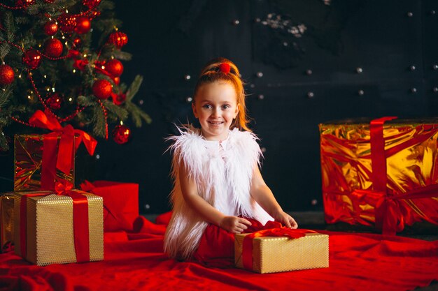 Kleines Mädchen, das Geschenk durch Weihnachtsbaum auspackt