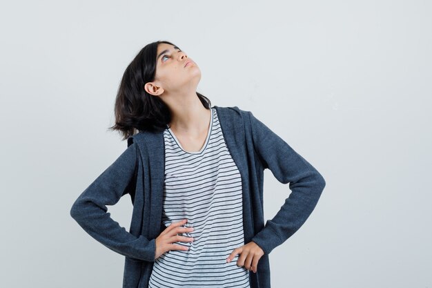 Kleines Mädchen, das Hände auf Taille im T-Shirt, in der Jacke hält und konzentriert schaut,