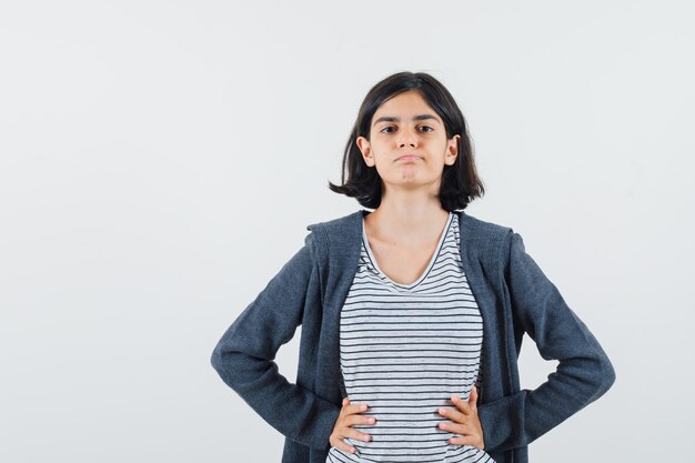 Kleines Mädchen, das Hände auf Taille im T-Shirt, in der Jacke hält und zuversichtlich schaut