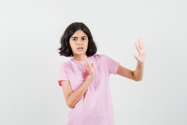 Kleines Mädchen, das Hände hält, um sich im rosa T-Shirt zu verteidigen und ängstlich aussieht, Vorderansicht.