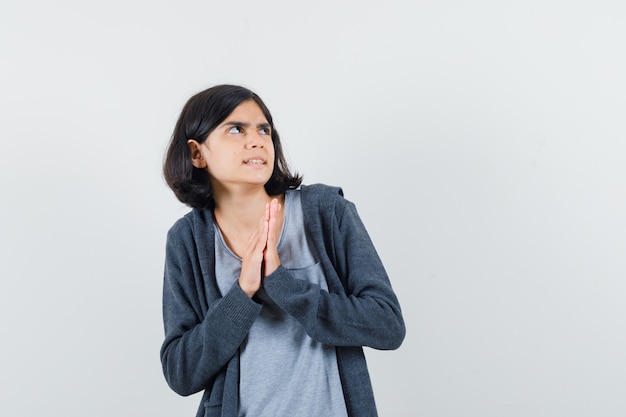 Kleines Mädchen, das Hände in der Gebetsgeste im T-Shirt, in der Jacke hält und ängstlich schaut,