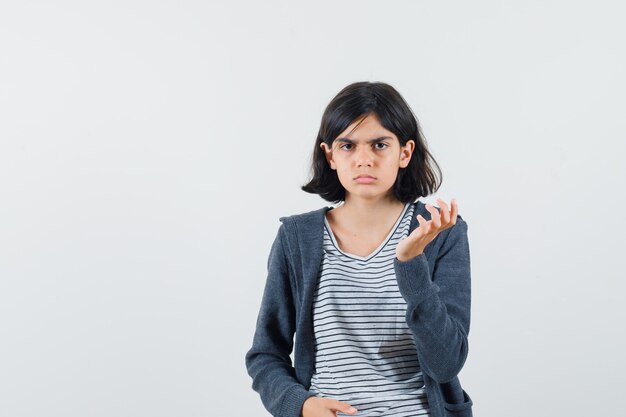 Kleines Mädchen, das Hand erhebt, während es im T-Shirt, in der Jacke aufwirft und ernst schaut