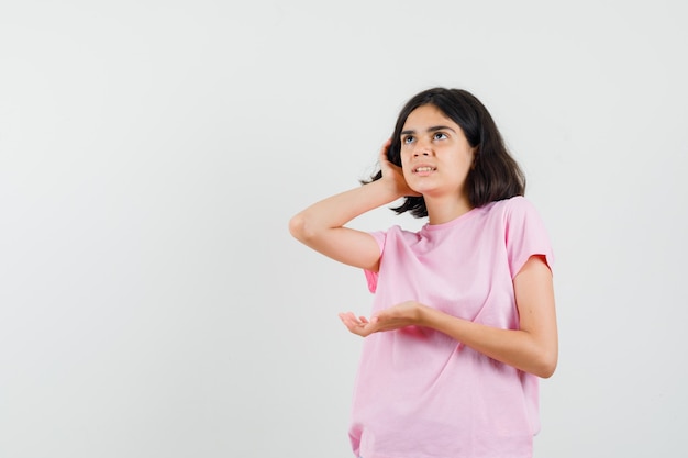 Kleines Mädchen, das Hand hinter Ohr im rosa T-Shirt hält und neugierige Vorderansicht schaut.