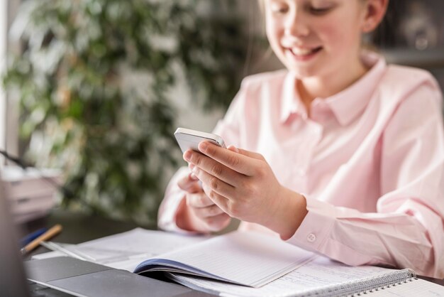 Kleines Mädchen, das ihr Telefon im Unterricht zu Hause überprüft