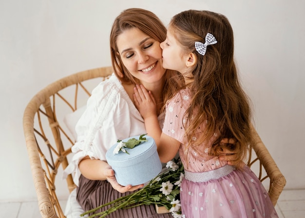 Kleines Mädchen, das ihre Mutter mit Frühlingsblumen und Geschenk überrascht