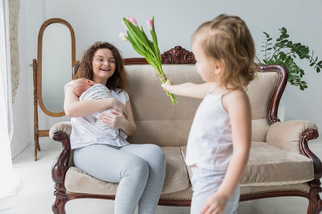 Kleines Mädchen, das ihrer lächelnden Mutter am Muttertag Tulpenblumen gibt