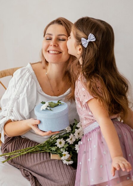 Kleines Mädchen, das ihrer Mutter Frühlingsblumen und Geschenkbox für Muttertag gibt