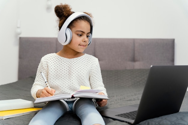 Kleines Mädchen, das Laptop und Kopfhörer für Online-Schule verwendet