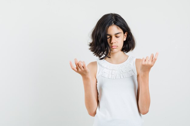 Kleines Mädchen, das Meditation mit geschlossenen Augen in der weißen Bluse tut und ruhig schaut. Vorderansicht.