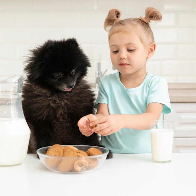 Kleines Mädchen, das Milch trinkt und mit Hund spielt