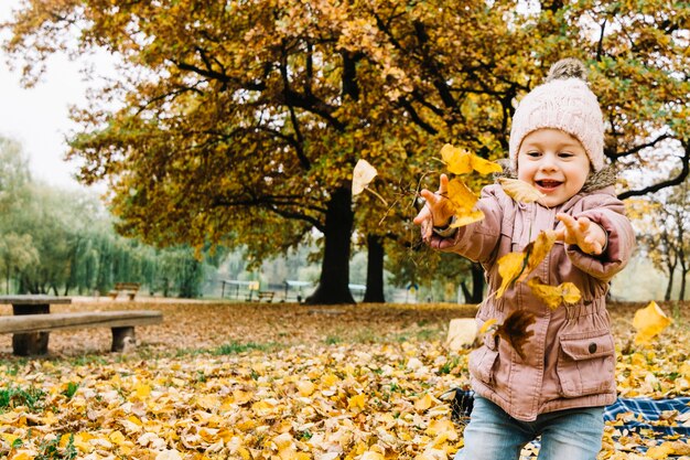 Kleines Mädchen, das mit Herbstblättern im Park spielt