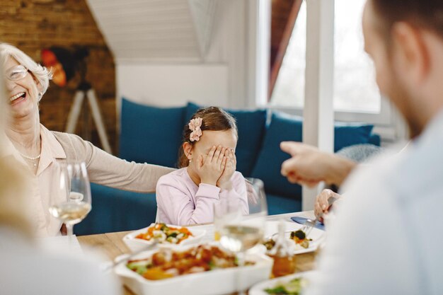 Kleines Mädchen, das mit ihrer Familie zu Mittag isst und ihre Augen bedeckt, während sie am Esstisch sitzt