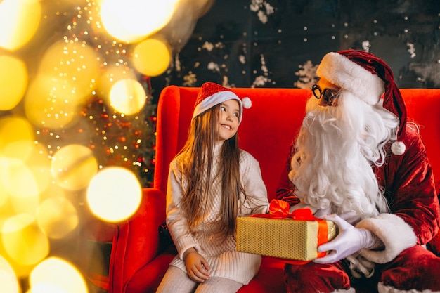 Kleines Mädchen, das mit Sankt und Geschenken auf Weihnachten sitzt