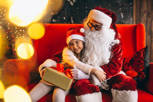Kleines Mädchen, das mit Sankt und Geschenken auf Weihnachten sitzt