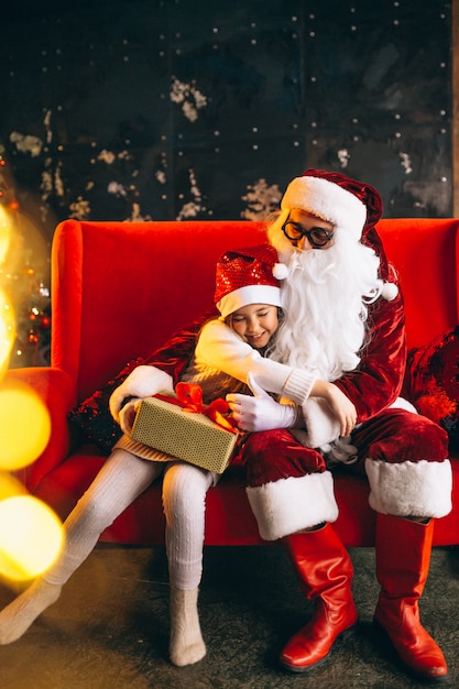 Kostenloses Foto kleines mädchen, das mit sankt und geschenken auf weihnachten sitzt