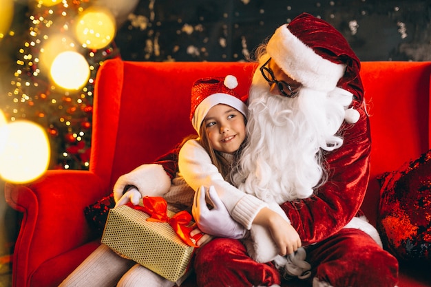 Kleines Mädchen, das mit Sankt und Geschenken auf Weihnachten sitzt