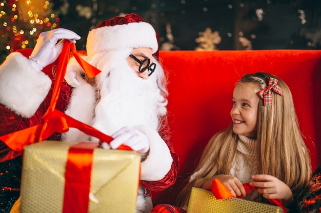 Kleines Mädchen, das mit Sankt und Geschenken auf Weihnachten sitzt
