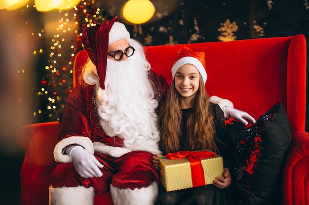 Kleines Mädchen, das mit Sankt und Geschenken auf Weihnachten sitzt