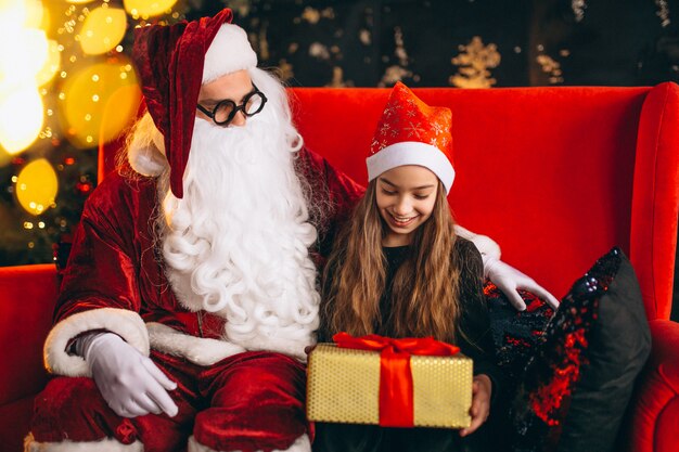 Kleines Mädchen, das mit Sankt und Geschenken auf Weihnachten sitzt