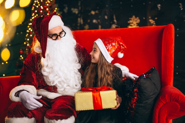 Kleines Mädchen, das mit Sankt und Geschenken auf Weihnachten sitzt