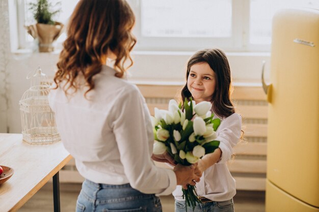 Kleines Mädchen, das Mutter mit Blumen am Muttertag begrüßt