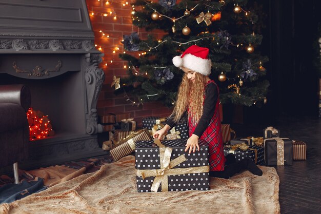 Kleines Mädchen, das nahe Weihnachtsbaum mit Geschenk steht