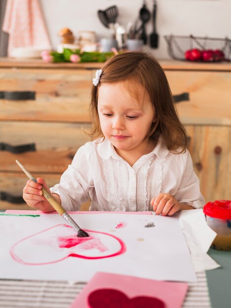 Kleines Mädchen, das rotes Herz auf Papier malt