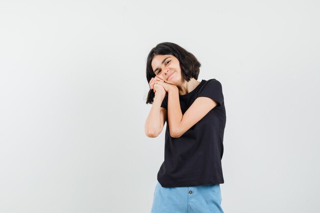 Kleines Mädchen, das sich auf gefaltete Hände als Kissen in schwarzem T-Shirt, Shorts stützt und reizend aussieht. Vorderansicht.