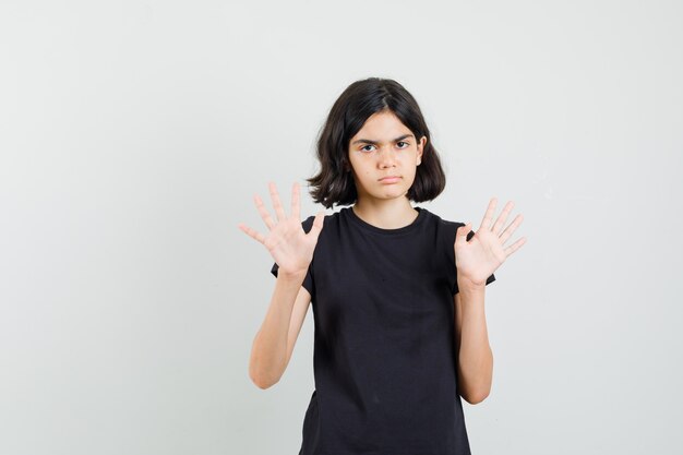 Kleines Mädchen, das Stoppgeste in schwarzem T-Shirt zeigt und genervte Vorderansicht schaut.