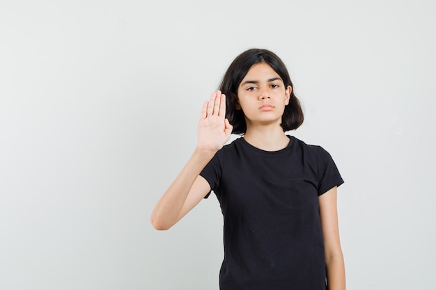 Kleines Mädchen, das Stoppgeste in schwarzem T-Shirt zeigt und genervte Vorderansicht schaut.