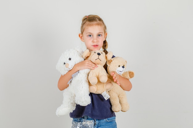 Kleines Mädchen, das Teddybären hält und Kamera in der Vorderansicht des T-Shirts und des Jeansrockes betrachtet.
