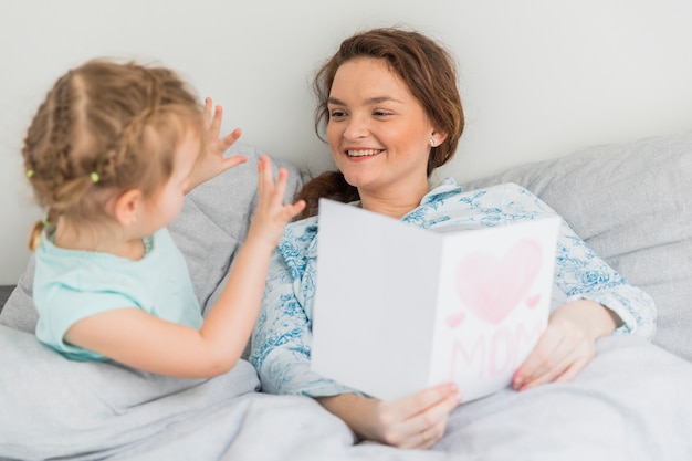 Kleines Mädchen, das vor ihrer Mutter auf Bett gestikuliert