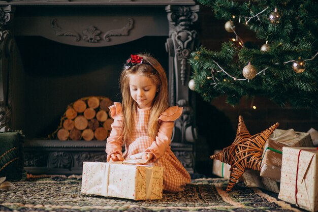 Kleines Mädchen, das Weihnachtsgeschenke durch Weihnachtsbaum auspackt