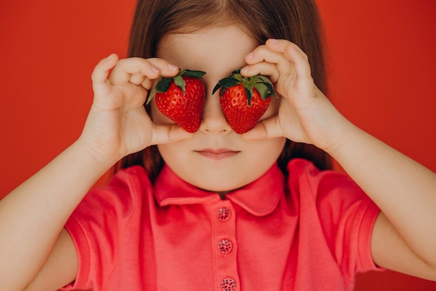 Kleines Mädchen, das zwei köstliche Erdbeeren hält