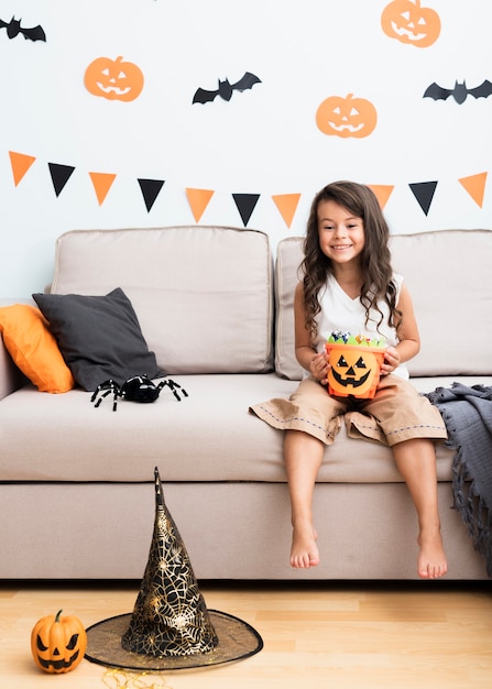 Kleines Mädchen der Vorderansicht, das auf Couch an Halloween sitzt